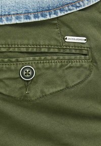 Tessuto verde oliva con una finitura texture, dotato di chiusura con bottone, una tasca con un'etichetta che reca la scritta "JACK & JONES," e denim nella parte superiore.