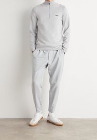 Sweat-shirt zippé gris clair avec épaules côtelées, assorti à un pantalon taper. Baskets blanches avec semelles en caoutchouc. Design minimaliste.