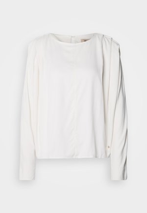 Valkoinen pitkähihaiseen toppi, jossa on pyöreä pääntie, pehmeä kangas, hillityt laskokset olkapäissä ja pieni kultainen yksityiskohta hihassa.