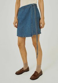 Denim wikkelrok in middelblauw met een rauwe zoom en zijdeeltail. gecombineerd met lichtbruine loafers en beige sokken.