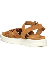 Tan suede sandaal met een geweven patroon op de teen, voorzien van kruissandalen en een witte, gevoerde zool voor comfort. Verstelbare enkelband.