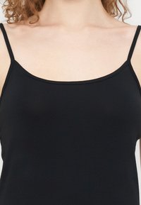 Μαύρο τοπ καμιζόλ με λεπτές τιράντες ώμου, φτιαγμένο από απαλό ύφασμα, με εφαρμοστή γραμμή και απλό, καθαρό σχέδιο στο ντεκολτέ.