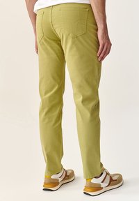 Pantaloni din bumbac oliv, cu croială slim-fit, dotati cu două buzunare posterioare și detalii cusute. Purtați cu adidași bej și galbeni.