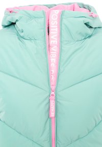 Helleblaue gepolsterte Jacke mit pinkem Reißverschlussanhänger, auf dem "BE HAPPY" steht, und innerem Reißverschlussflap, auf dem "POSITIVE VIBES" gedruckt ist.