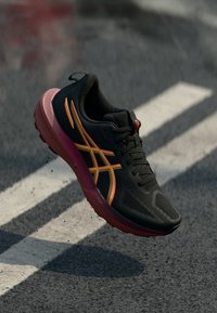 Baskets de course noires avec une tige texturée, des accents orange et jaune, et une semelle rose ; disposent d'un laçage traditionnel et d'un design rembourré.