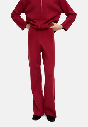 Czerwone dzianinowe spodnie w kształcie dzwonów z bezszwowym pasem, charakteryzujące się miękką teksturą i luźnym krojem, w zestawie z pasującą bluzką.