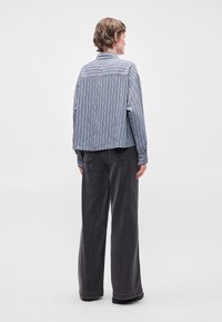 Stribet blå og grå skjorte med knapper og afslappet pasform, parret med brede sorte bukser, vist fra bageste udsigt og med minimale detaljer.