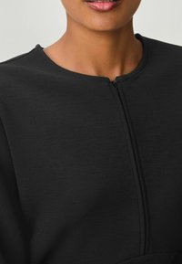 Abito nero con zip anteriore, caratterizzato da un collo arrotondato, tessuto strutturato e dettagli delle cuciture. Il design mette in risalto una silhouette aderente.