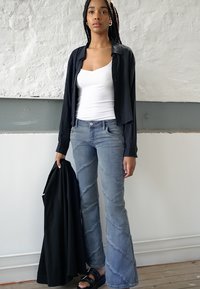 Camisa preta de botões sobre uma camiseta branca, combinada com jeans claros de boca de sino com costura diagonal. Sandálias pretas e uma jaqueta preta.