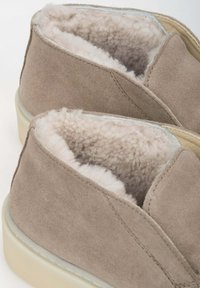 Beige suède instappers met een zachte, lichtgekleurde fleece voering en een lichte rubberen zool. Inclusief stiksels rond de randen.