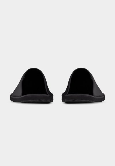 Ζεύγος μαύρων σανδαλιών χωρίς λουριά με κλειστά δάχτυλα και υφηλικές σόλες, εμφανίζεται από μπροστινή γωνία σε απλό ανοιχτό φόντο.