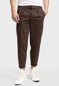 Ruskeat chino-housut, joissa on rento malli, käännetyt lahkeet ja hopeaketju sivussa, valmistettu kevyestä kankaasta.