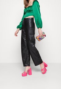 Zelená saténová blůza s nabíranými rukávy, široké černé kožené kalhoty, růžové platformové boty a barevná vzorovaná kabelka.
