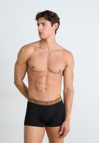 Boxers en coton noir avec une ceinture marron arborant le logo "TOMMY HILFIGER". Le tissu semble lisse et ajusté.