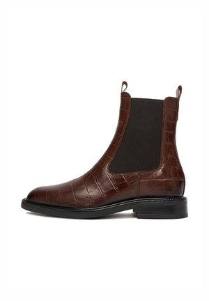 Bottine Chelsea en cuir marron au motif crocodile avec des panneaux élastiques sur les côtés, bout rond et un petit talon empilé. Semelle plate pour la stabilité.