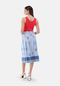 Rotes ärmelloses Oberteil mit V-Ausschnitt, kombiniert mit einem hellblauen Rock mit bunten gedruckten Figuren und einem gestreiften Saum. Weiße Blockabsätze.