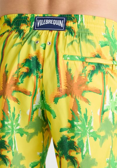 Shorts de bain jaunes avec un motif de palmier vert et orange. Comprend une taille élastique, une poche arrière et des œillets de drainage.