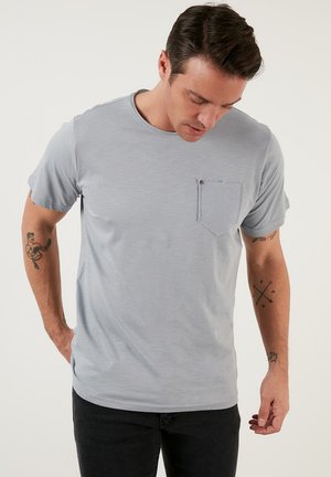 T-shirt grigio chiaro a maniche corte con scollatura rotonda, dotato di taschino sul lato sinistro del petto e una texture liscia.