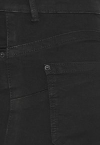Black denim pants featuring a smooth texture, side pocket detail with metal accent, and subtle stitching patterns along the seams.