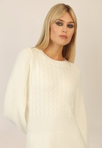 Weißer gestrickter Pullover mit einem Zopfmuster im oberen Bereich, Rippbund und weiten Ärmeln. Glatte Textur mit lockerer Passform.