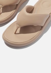 Beige teenslippers met een textuur van leer aan de bovenkant, ontwerp met teenpost en een gekussende zool. Afgeronde rand en minimale stiksels.
