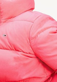 Světle růžová péřová bunda s prošívaným vzorem. Obsahuje logo nášivku, vysoký límec a hladkou, matnou texturu.