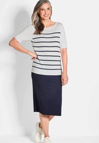 Lichtgrijze gebreide top met marineblauwe strepen, korte mouwen, gecombineerd met een effen marineblauwe rok tot de knie en witte sneakers.