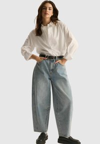 Biała koszula z guzikami i podwiniętymi rękawami, w połączeniu z jasnoniebieskimi, wysoko taliowanymi spodniami o szerokich nogawkach i czarnym paskiem. Czarne szpilki.