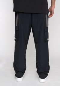 Pantaloni cargo neri con molte tasche, strisce laterali grigie e una vestibilità rilassata. Presentano un tessuto testurizzato e un logo sulla tasca sinistra.