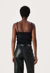 Mustast kunstkarusnahast crop top, millel on reguleeritavad rihmad, koos kõrge vöökohaga mustade nahkpükstega, millel on tagumised taskud ja CK logo detail.