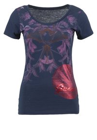 Camisa de manga corta color azul marino con diseños florales y abstractos en púrpura, que presenta un gran círculo rojo brillante con el texto "Guess" en la parte inferior derecha del frente.