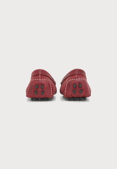 Paire de mocassins en daim rouge avec couture blanche et semelles en caoutchouc noir au talon, vus de dos sur un fond blanc uni.