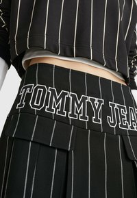 Zwart gestreepte skort met een brede tailleband waarop "TOMMY JEANS" in witte letters staat, gemaakt van een gestructureerde stof met een geplooid ontwerp.