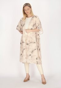 Lettet, beige kimono med grå blomsterprint, åben frontdesign, brede ærmer, parret med cremede leggings og brune hæle.