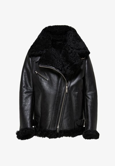 Musta nahkatakki, jossa on pörröinen musta shearling-kaulus ja hihansuut, joissa on hopeiset vetoketjut, vino etuvetoketju ja solkikoristeet.