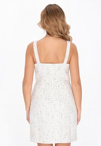 Fehér ruha textúrált anyagból, rácsos mintázattal, négyzet alakú dekoltázzsal, széles pántokkal és feszes derékkal, a térd fölött végződik.