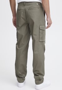 Pantaloni cargo din bumbac verde oliv, cu croială lejeră, buzunare laterale și talie elastică. Asortați cu adidași albi.