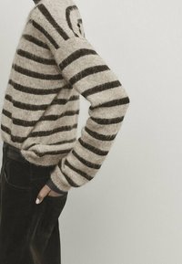 Sweter w paski w odcieniach beżu i ciemnego brązu, wykonany z miękkiego materiału, z długimi rękawami i luźnym krojem oraz ściągaczami przy mankietach.