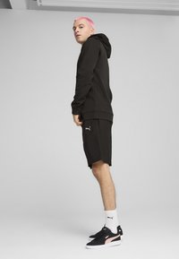 Den sorte hættetrøje har en kengurulomme og ribbede manchetter. Sammen med sorte shorts og sorte sko med pink detaljer. Hvide sokker er synlige.