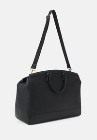 Sac de voyage en cuir noir avec double poignées et une bandoulière réglable, présenté sur un fond blanc uni.