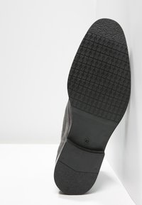 Sole of a black men's shoe with textured tread pattern and size 42 marking, positioned upright against a white corner background.