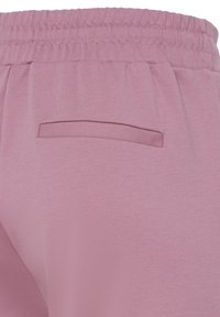 Približen posnetek roza hlač z elastičnim pasom in zadnjim žepom z ravnim šivom brez vidnega zapiranja.