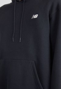 Sweat à capuche en coton bleu marine foncé avec une poche kangourou à l'avant et un petit logo blanc brodé sur la poitrine gauche. Tissu texturé.