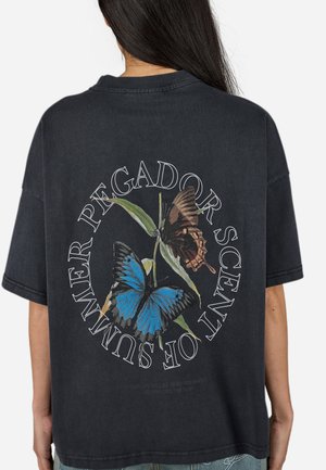 Tricou negru oversized cu un grafic de fluturi albaștri și maronii, având textul "PEGADOR SCENT OF SUMMER" aranjat circular.