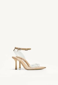 Transparente High-Heelsandalen mit einer beigen Sohle, dünnen transparenten Riemen und einem zierlichen Knöchelriemen mit einer metallischen Schnalle.