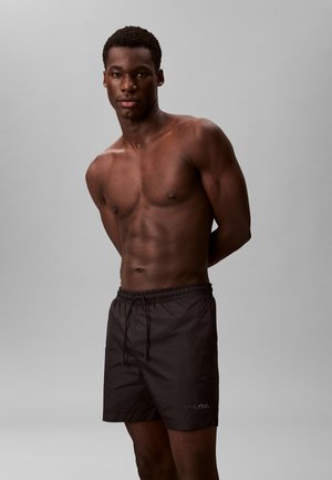 Shorts de bain noirs avec une taille élastique et un cordon de serrage. Fabriqués en matériau léger. Logo affiché sur la jambe gauche.