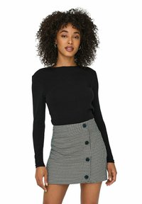 Top nero a maniche lunghe abbinato a una gonna a motivo houndstooth con sei bottoni neri sul davanti e una silhouette aderente.