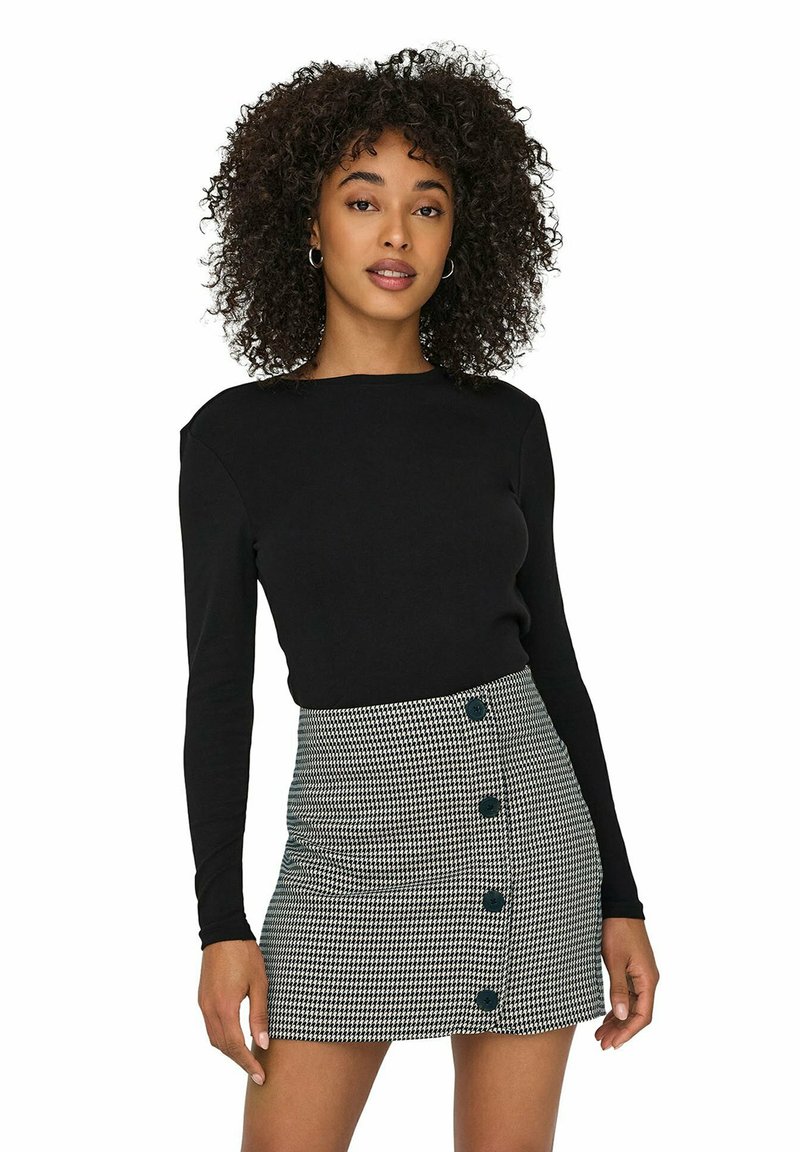 Top nero a maniche lunghe abbinato a una gonna a motivo houndstooth con sei bottoni neri sul davanti e una silhouette aderente.