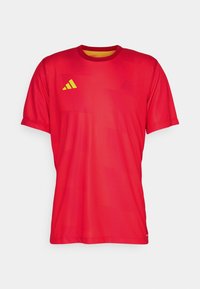 Röd sportt-shirt med korta ärmar, tillverkad av lättviktsmaterial. Har en gul logotyp på bröstet och subtila mönster i texturen.