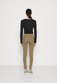 Black long-sleeve cropped top paired with fitted olive green leggings and light sneakers, viewed from the back against a plain background.
